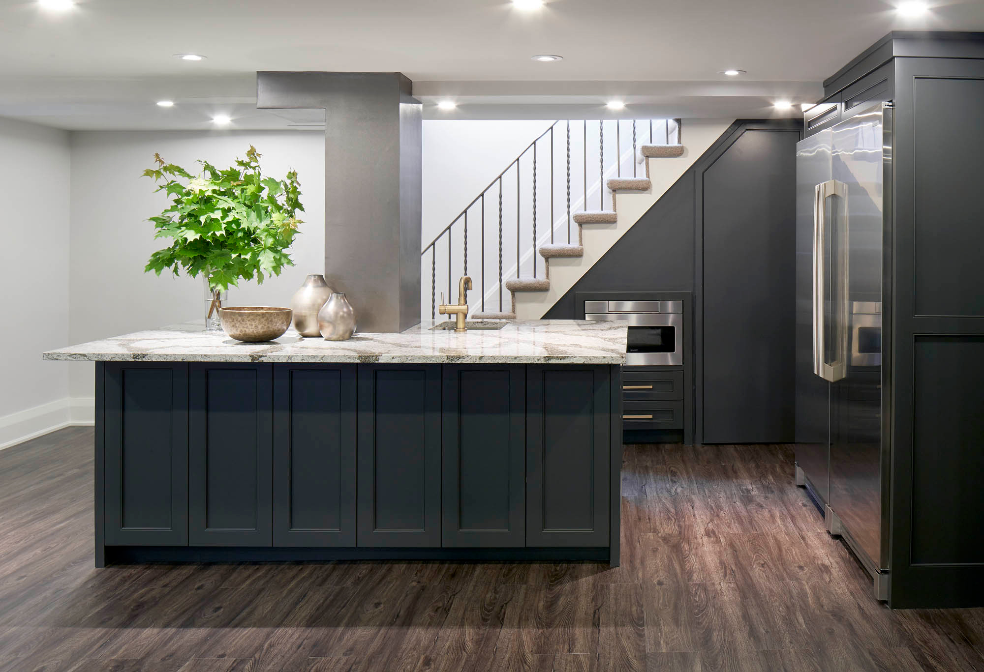 NUITH – FIFTY SHADES OF DIOR GRAY – BASEMENT MANCAVE KITCHENETTE DESIGNED BY CELIA ALIDA RUTTE – PHOTOS BY DONNA GRIFFITH A basement kitchenette with white counter and dark grey cabinets built into the stairs and surrounding area making maximum use of the space.