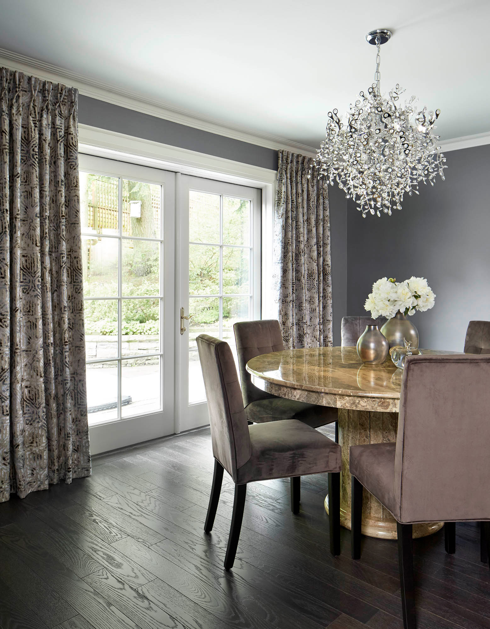 NUITH – FIFTY SHADES OF DIOR GRAY – DINING ROOM DESIGNED BY CELIA ALIDA RUTTE – PHOTOS BY DONNA GRIFFITH A dining room designed in shades of purple grey, with a large round stone table, dining chairs, floor to ceiling drapery and a chrystal chandelier.