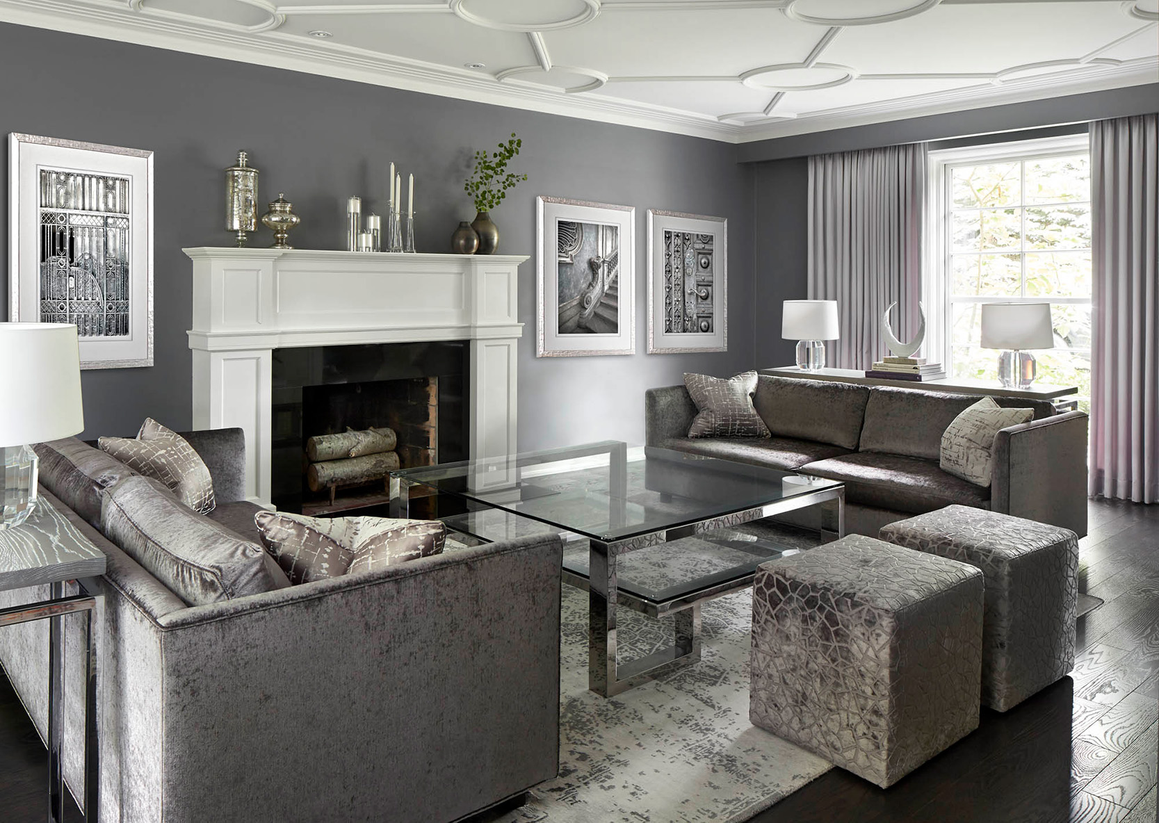 NUITH – FIFTY SHADES OF DIOR GRAY – LIVING ROOM DESIGNED BY CELIA ALIDA RUTTE – PHOTOS BY DONNA GRIFFITH A living room designed in shades of purple grey, with two sofas, two square ottomans, a large square glass coffee table, and a large white fireplace mantle.
