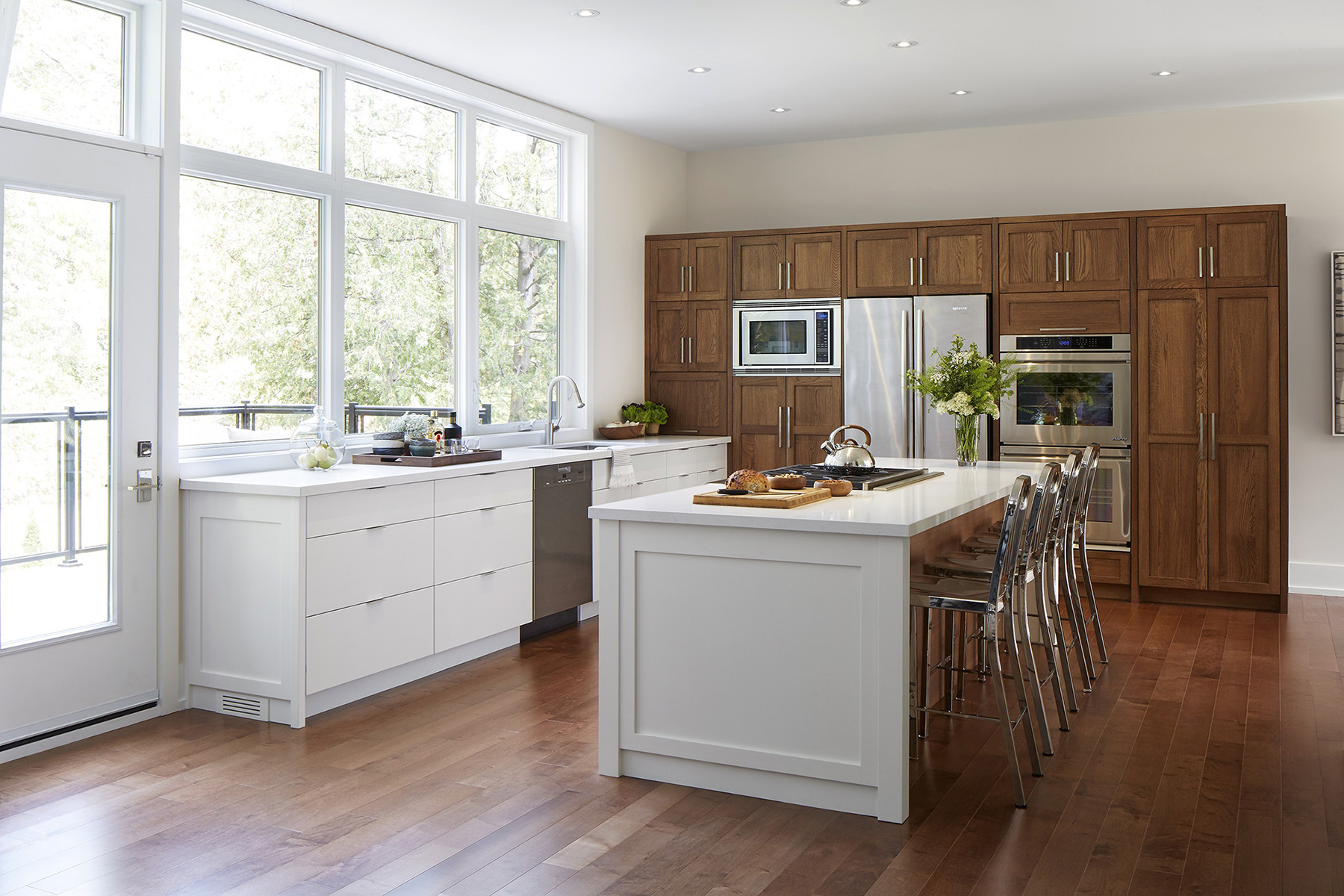 NUITH – THE GREAT GRIMSBY – MODERN KITCHEN DESIGNED BY CELIA ALIDA RUTTE – PHOTO BY DONNA GRIFFITH A wide-angle photo of a modern kitchen designed with warm midtone woods, white countertops, high gloss white cabinets and a large picture window.