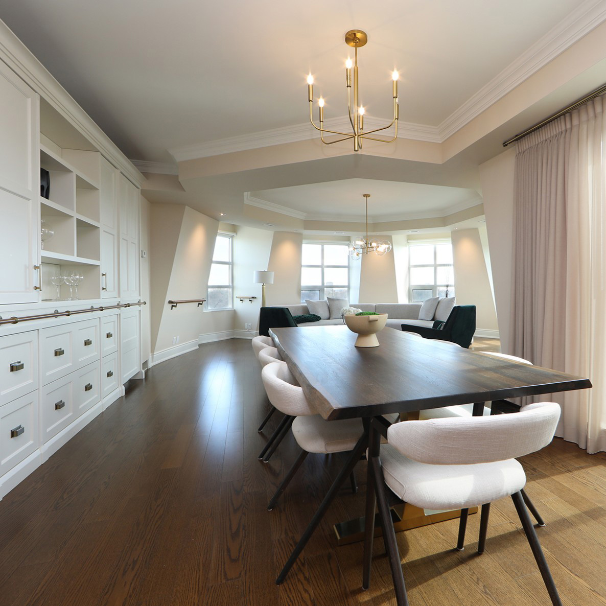 A condo interior with a large circular living room, custom cabinetry, floor to ceiling drapery panels, and modern furniture.