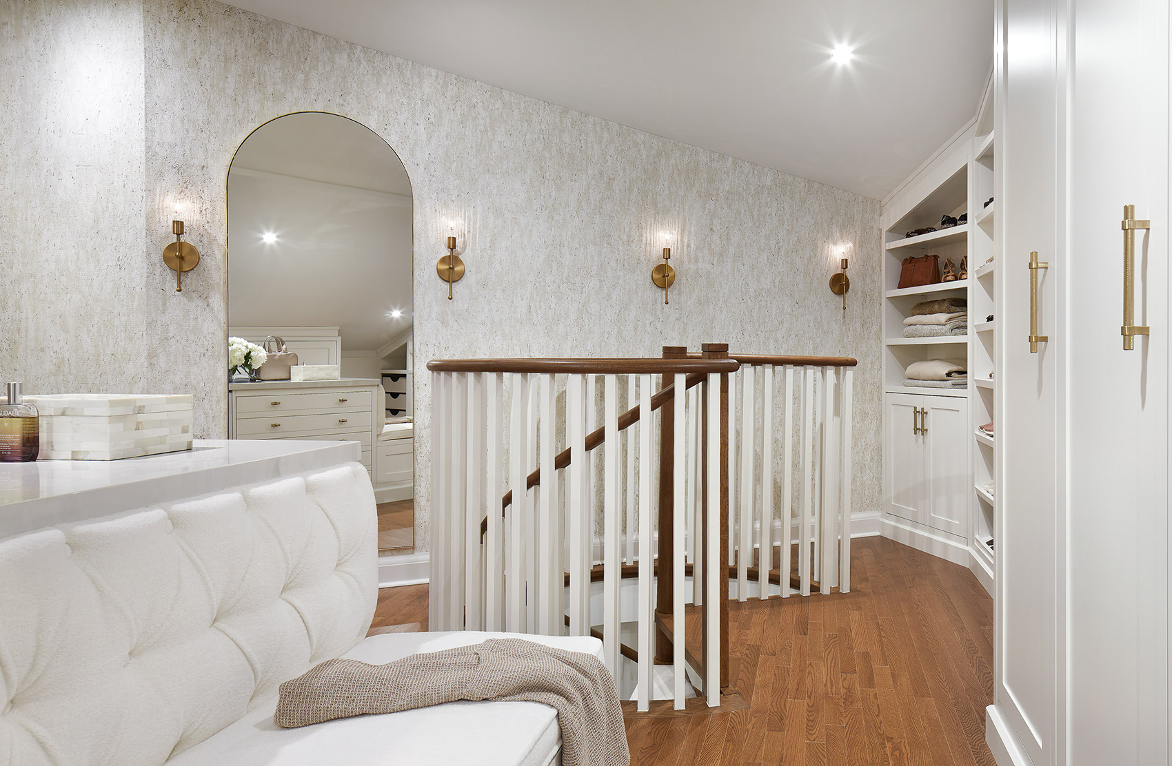 A spiral staircase leading up to an attic room that has been transformed into a beautiful walk in closet designed in layered textures of off white and warm brass accents.