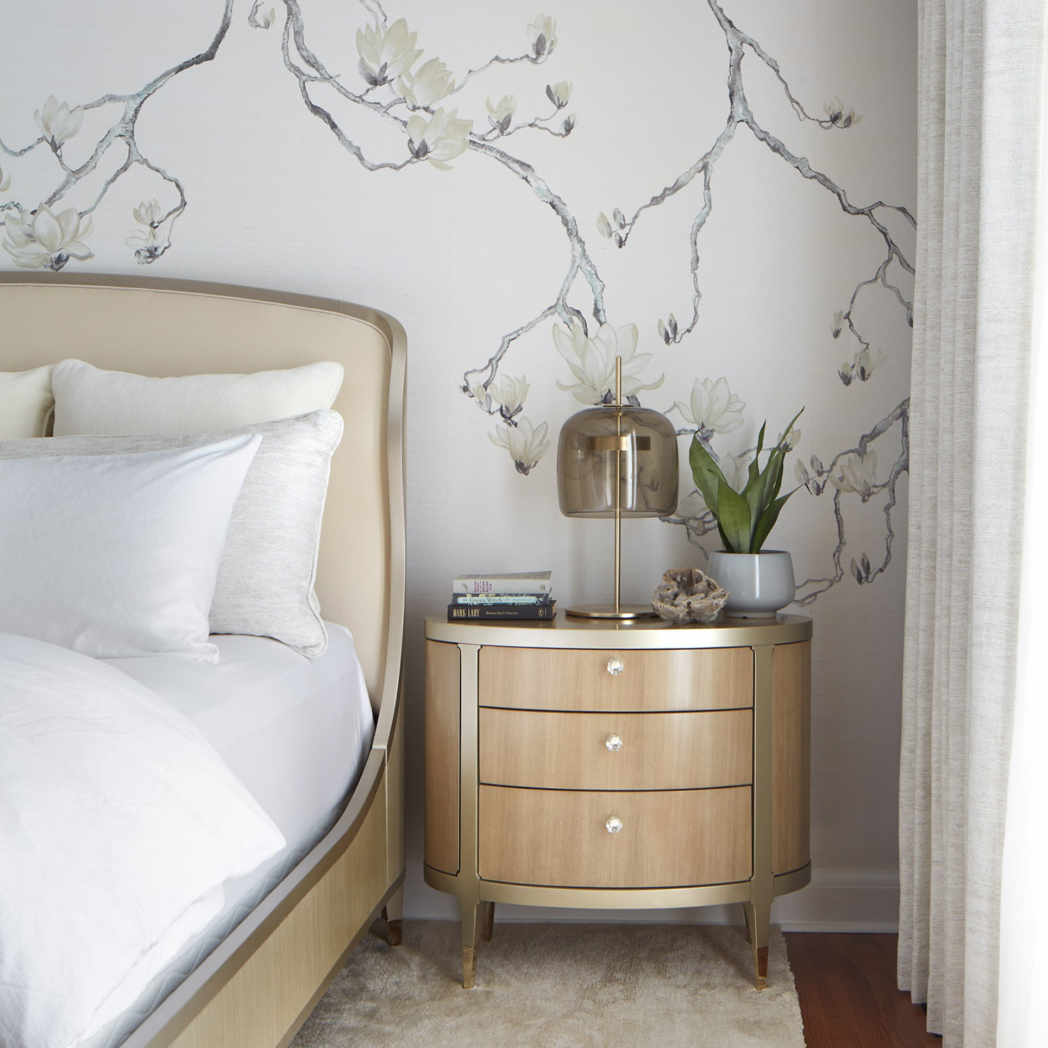 Multiple photos in a carousel showing a bedroom in soft off white colours with beautifully styled and folded down bed sheets and a bedframe and nightstand in soft curved forms.