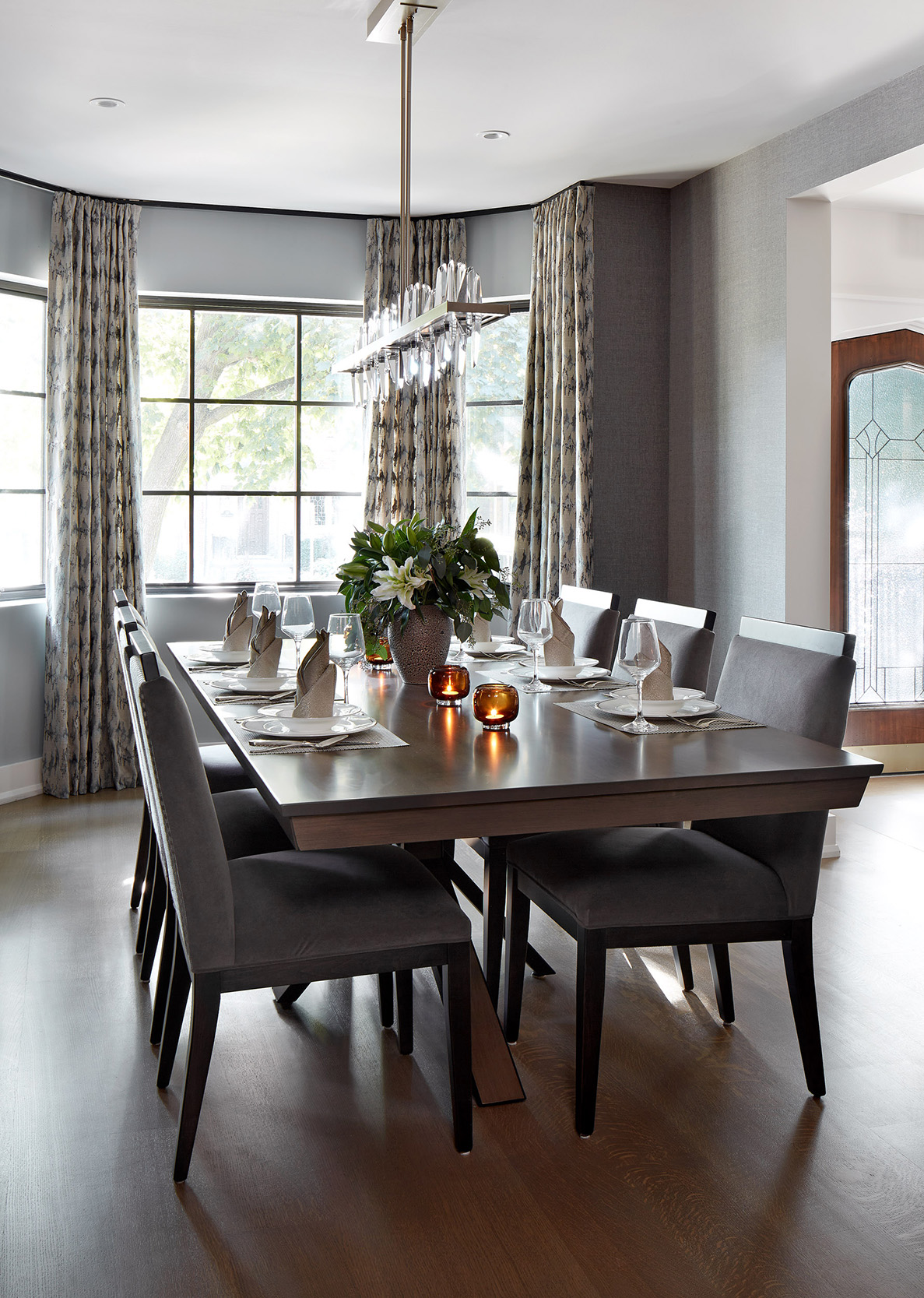 NUITH – ENLIGHTENED BY A TEMPEST – DINING ROOM DESIGNED BY CELIA ALIDA RUTTE – PHOTO BY DONNA GRIFFITH dining room designed with warm woods, gray purple chair fabrics, a textured natural grass cloth wallpaper and a stunning modern linear crystal chandelier.
