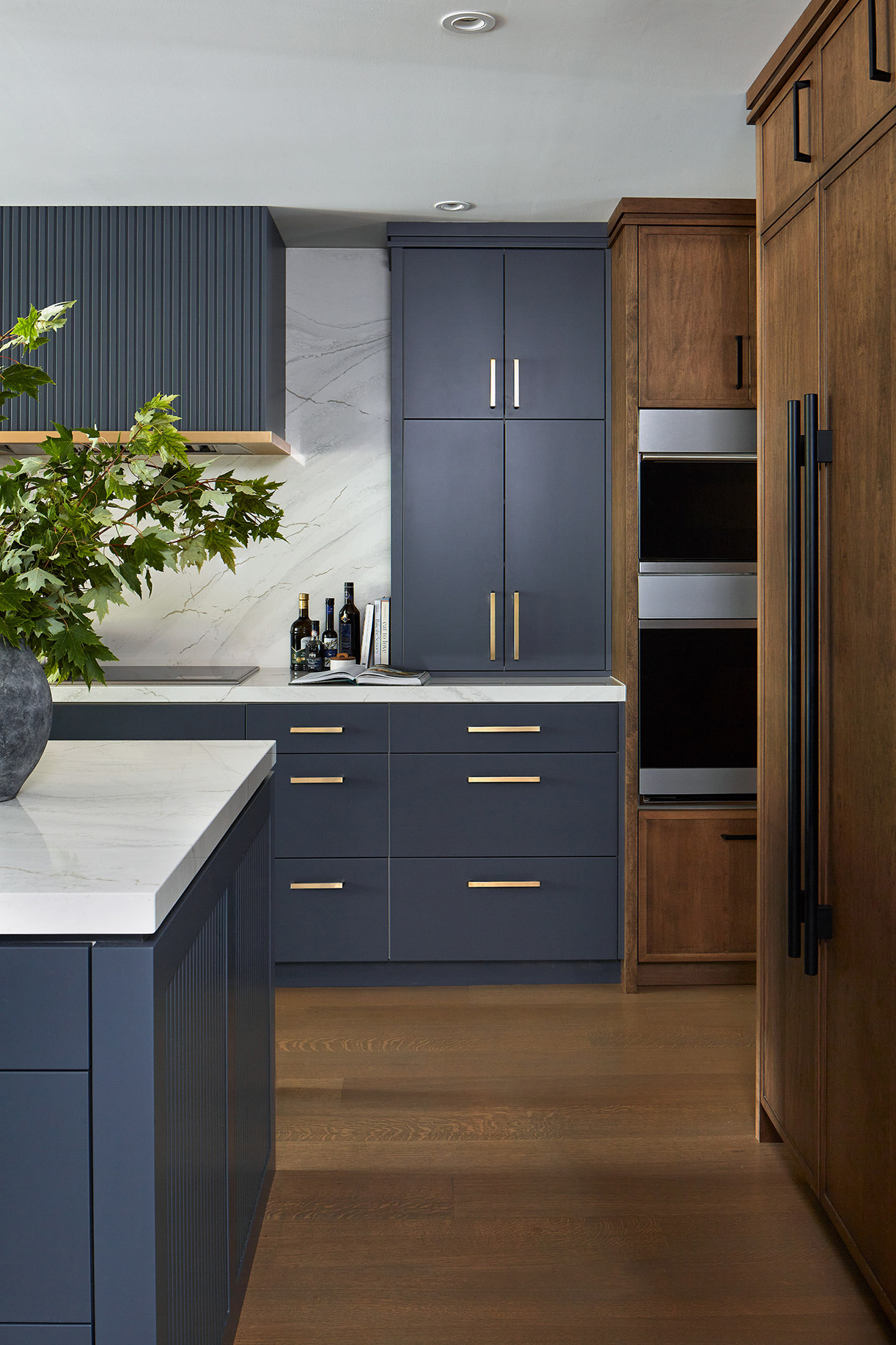 NUITH – ENLIGHTENED BY A TEMPEST – KITCHEN DESIGNED BY CELIA ALIDA RUTTE – PHOTO BY DONNA GRIFFITH A kitchen designed with a combination of warm woods and deep gray blue cabinetry design with brass and matt black handles.